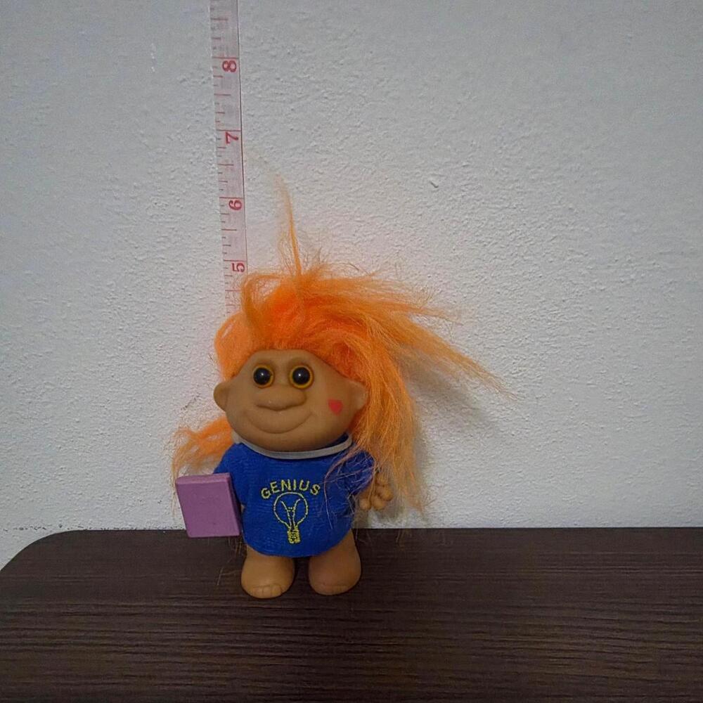 Orange-haired troll doll with blue shirt featuring yellow 'GENIUS' text and ligh